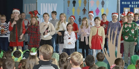 Powiększ grafikę: Śpiewające i pokazujące językiem migowym śpiewane słowa dzieci z klasy IV stojące na scenie