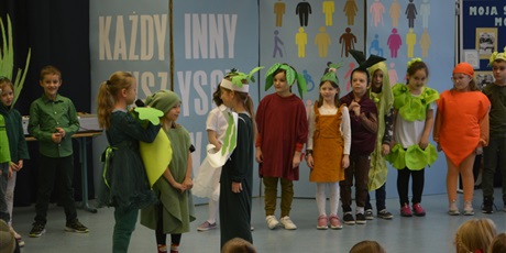 Powiększ grafikę: Dzieci z klasy I ubrane w stroje przypominające różne warzywa stoją na scenie i recytują wiersz.