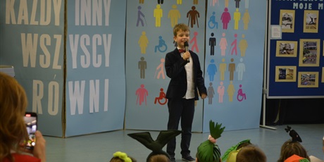 Powiększ grafikę: Uśmiechnięty chłopiec z klasy III stoi na scenie z mikrofonem i recytuje wiersz.