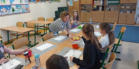 Powiększ grafikę: Nauczyciel z dziećmi w sali lekcyjnej przy ławkach wykonują prace plastyczne 