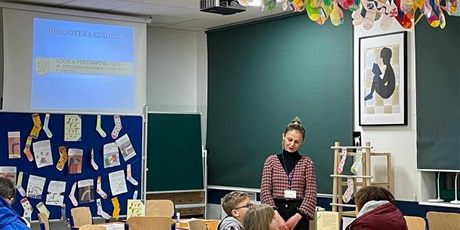 Powiększ grafikę: Biblioteka szkolna: nauczyciel bibliotekarz przemawia do dzieci i rodzica siedzących w ławkach