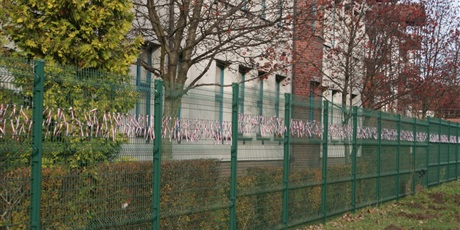 Powiększ grafikę: dekoracja z biało-czerwonych wstążek na płocie wokół budynku szkoły wykonana przez dzieci z wychowawcami z okazji uroczystości 11 listopada