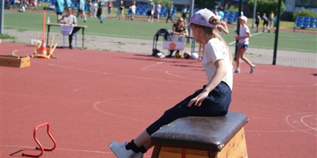 Powiększ grafikę: Dziewczynka siedzi na skrzyni na boisku szkolnym