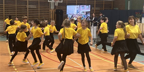 Powiększ grafikę: Zespół młodych tancerzy: dziewczynki i chłopcy w żółtych koszulkach tańczą na sali gimnastycznej