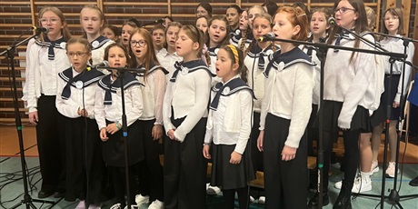 Powiększ grafikę: chór śpiewa - dziewczynki ubrane w białe bluzki z granatowym marynarskim kołnierzu, stoją i śpiewają 