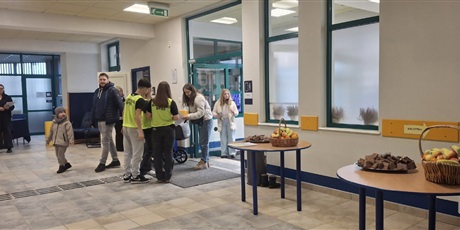 Powiększ grafikę: Wejście główne do szkoły. Uczniowie witają wchodzących rodziców z dziećmi.