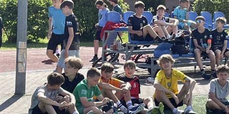 Powiększ grafikę: chłopcy odpoczywają po meczu - siedzą na boisku szkolnym: na trybunach i na trawie.