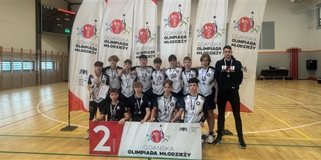 Powiększ grafikę: Dryżyna 12 chłopców z trenerem stoi na sali gimnastycznej i pozuje do zdjęcia z medalami i dyplomem