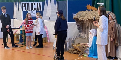 Powiększ grafikę: Na scenie policjantka na hulajnodze, lekarka w białym fartuchu, Maryja i Józef, w tle stajenka, dalej banner Policja oraz inni aktorzy