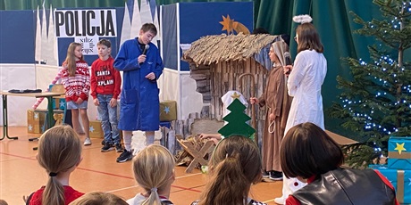 Powiększ grafikę: Widać publiczność z tyłu. Na scenie aktorzy, w tle komisariat, stajenka, najbliżej anioł 