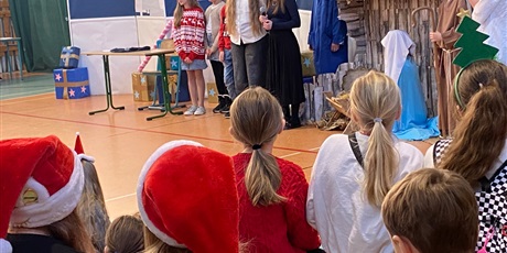 Powiększ grafikę: Widać publiczność z tyłu. Na scenie aktorzy, w tle komisariat, stajenka, najbliżej anioł 