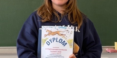 Powiększ grafikę: Portret - dziewczynka w okularach w granatowej bluzie stoi z dyplomem w rękach