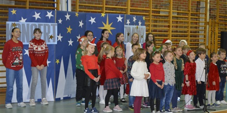 Powiększ grafikę: Dzieci stojące na scenie w sali gimnastycznej podczas koncertu świątecznego - chór szkolny 