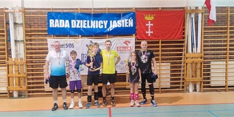 Powiększ grafikę: 3 dzieci i 3 dorosłych stoi w sali gimnastycznej z pucharami i medalami na szyi 