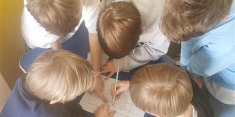 Powiększ grafikę: Zdjęcie z góry - 5 głów uczniów nad biurkiem.  jeden z nich pisze ołówkiem na kartce ołówkiem