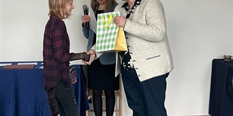 Powiększ grafikę: pani wicedyrektor wręcza nagrodę dziewczynce, obok stoi prowadząca z dyplomem i mikrofonem 