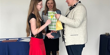 Powiększ grafikę: pani wicedyrektor wręcza nagrodę dziewczynce, obok stoi prowadząca z dyplomem i mikrofonem 