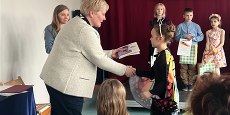Powiększ grafikę: pani wicedyrektor wręcza dyplom dziewczynce, obok stoją na scenie inni laureaci konkursu.