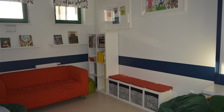 Powiększ grafikę: Biblioteka. Czerwona kanapa dwuosobowa i półki na zabawki w kąciku do wypoczynku